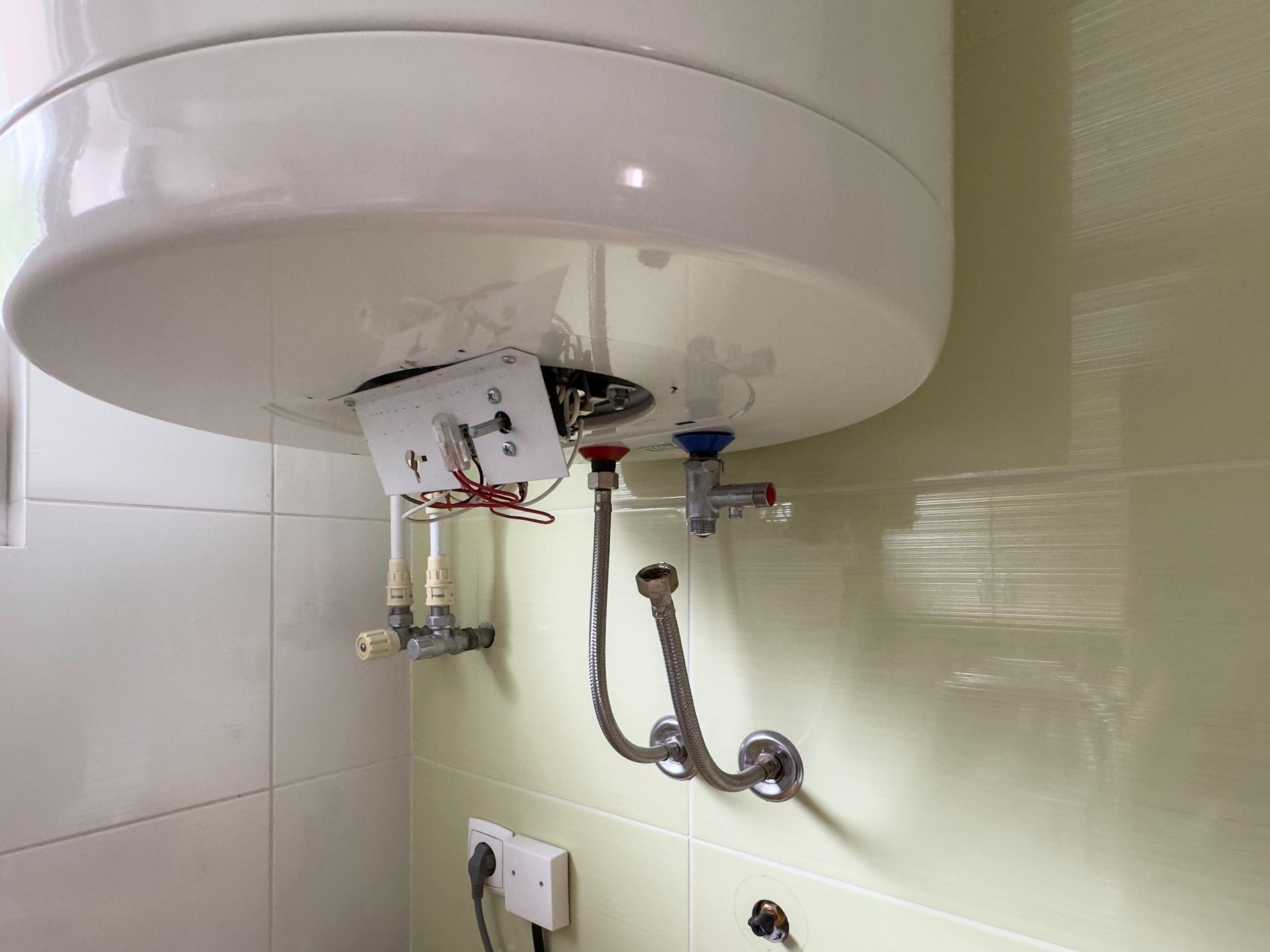 White water heater, pipes, and electrical components mounted on a tiled wall — D & E Milner Plumbing In The Palms, QLD