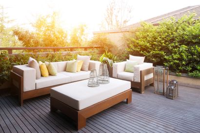 Patio avec mobilier d'extérieur beige, terrasse en bois et soleil éclatant.