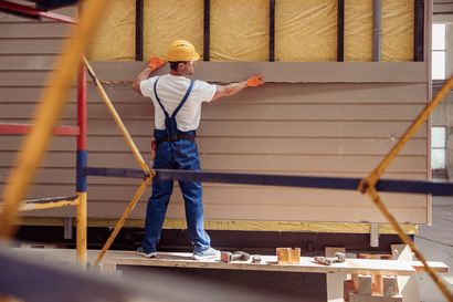 Ouvrier du bâtiment installant un revêtement en bois sur un mur, portant un casque de sécurité et un équipement de sécurité.