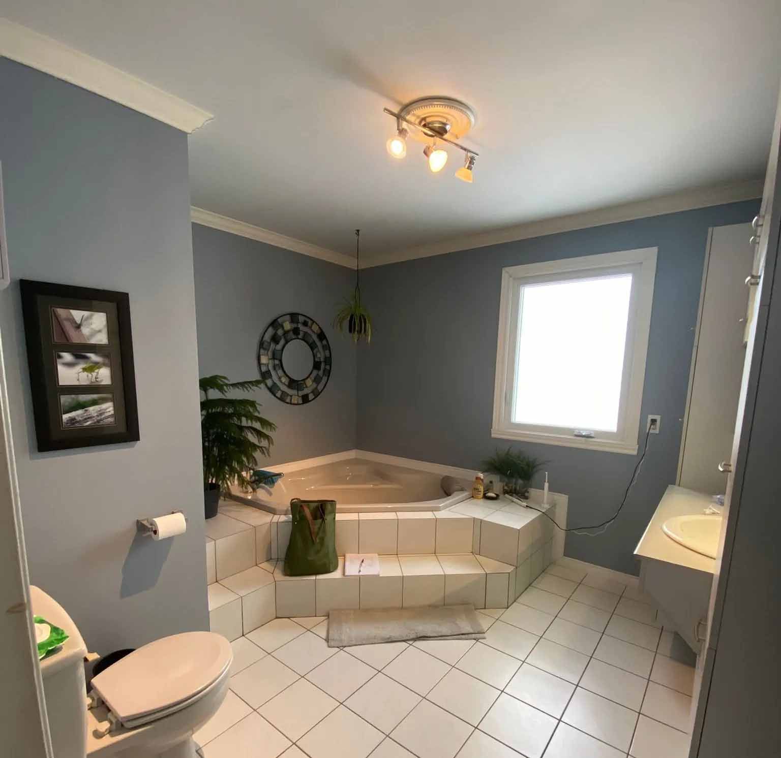 Salle de bain avec baignoire jacuzzi d'angle, murs bleus et sol carrelé blanc.