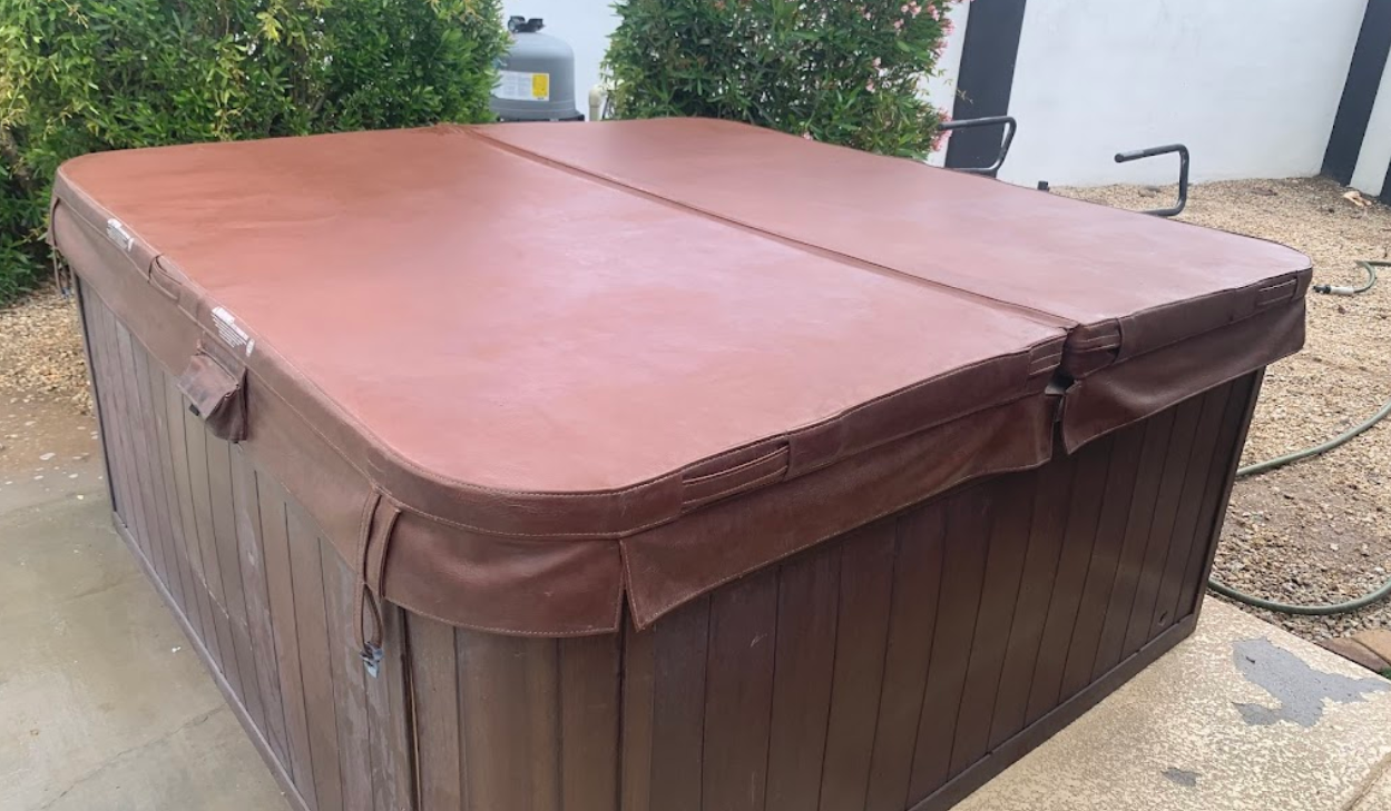 A wooden hot tub with a red cover is sitting on the ground.