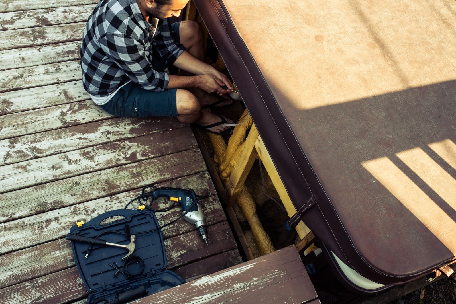 A man is sitting on a wooden deck working on a hot tub.
