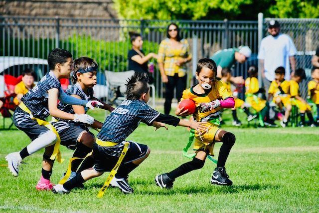 Children playing tag on a grassy field, with one child in a yellow shirt running while others reach to tag them.