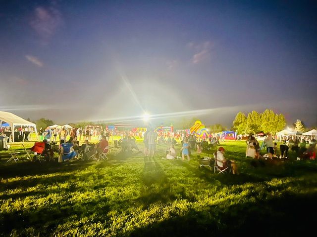 Sunlit outdoor festival on a grassy field with crowds, tents, and bright lens flare