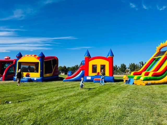 Colorful inflatable bounce houses and slides on a grassy field under a bright blue sky.