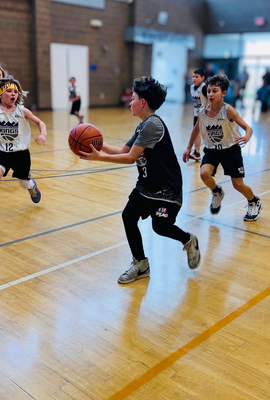 Youth basketball players dribble and defend on an indoor court during a game