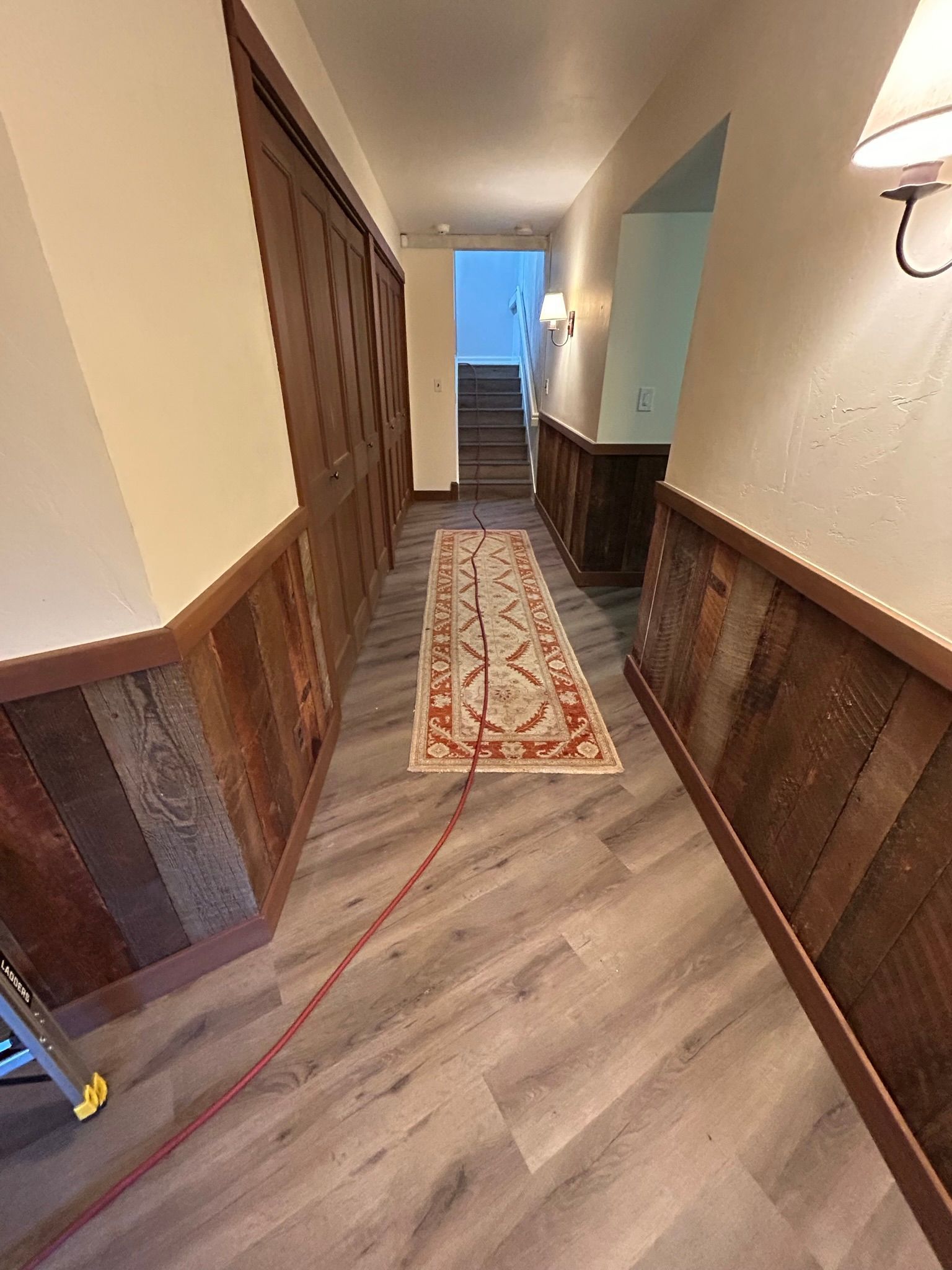 Hallway with wood paneling, gray floor, beige rug, and brown door.