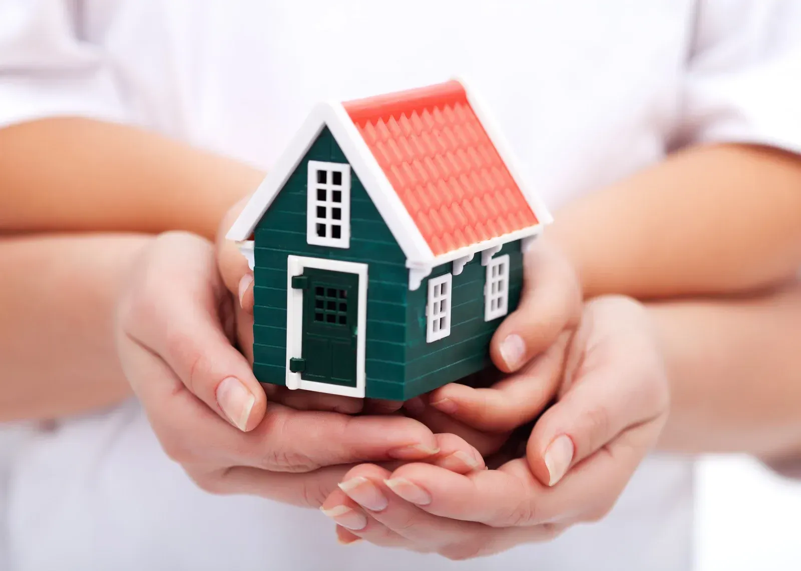 Hands holding a miniature green house with a red roof.