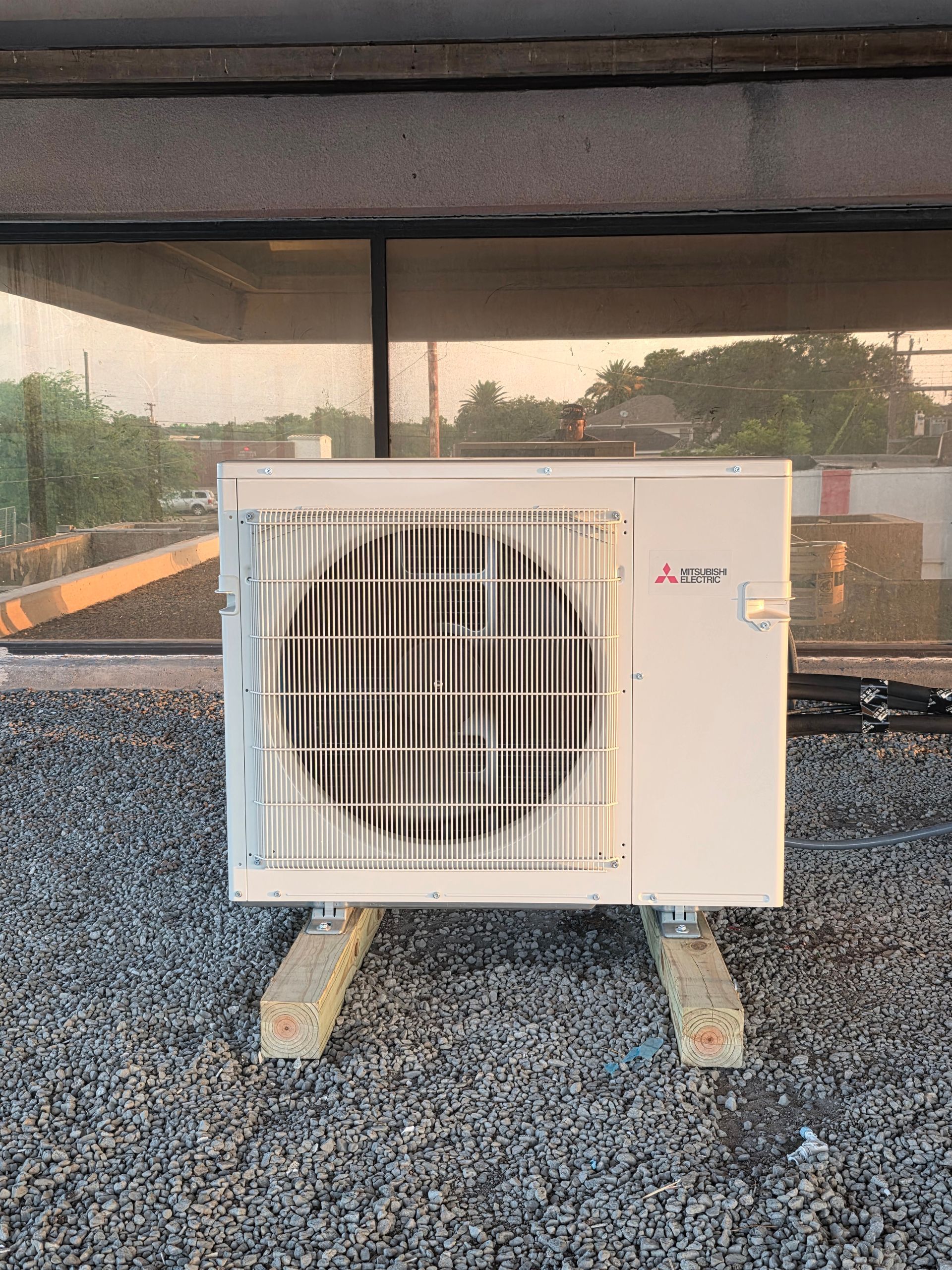 White air conditioning unit mounted on wooden blocks on a gravel rooftop.