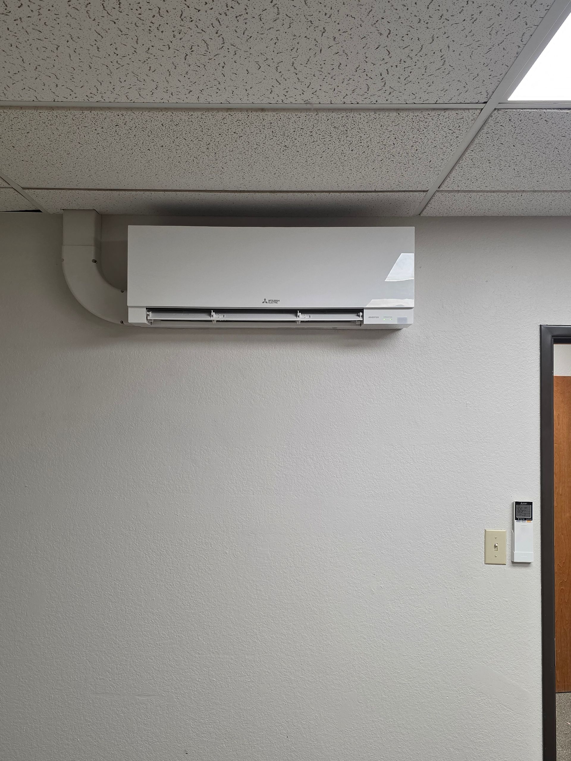 White wall-mounted air conditioner on a textured wall, near a door and ceiling tiles.