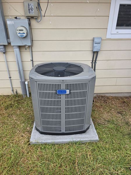 An air conditioning unit on a concrete pad outside a building with siding.
