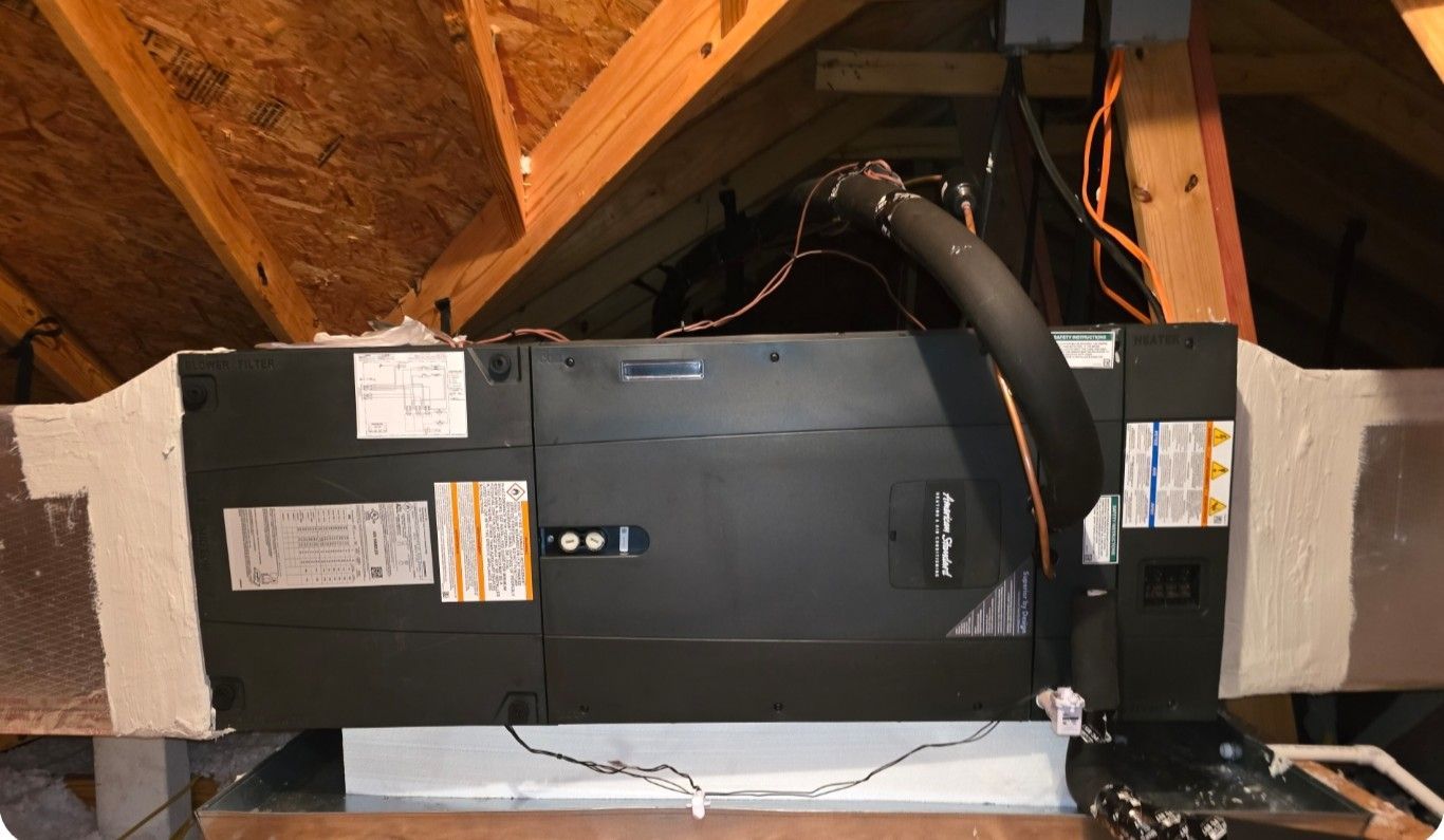 HVAC unit in attic, dark metal with black insulated tubing and ductwork; wooden beams.