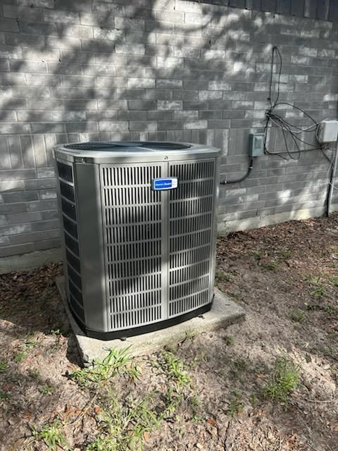 Air conditioning unit on a concrete slab against a gray cinder block wall.