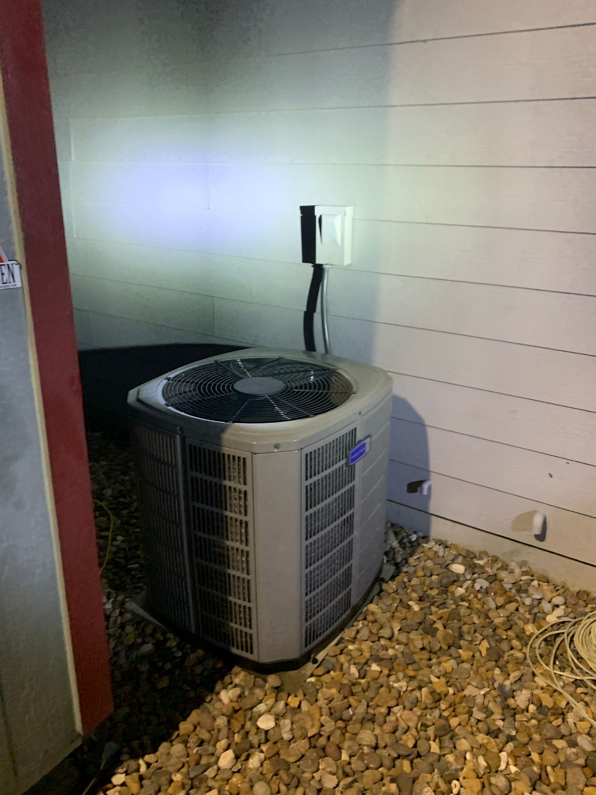 Air conditioning unit next to a light-colored wall with a gravel base.