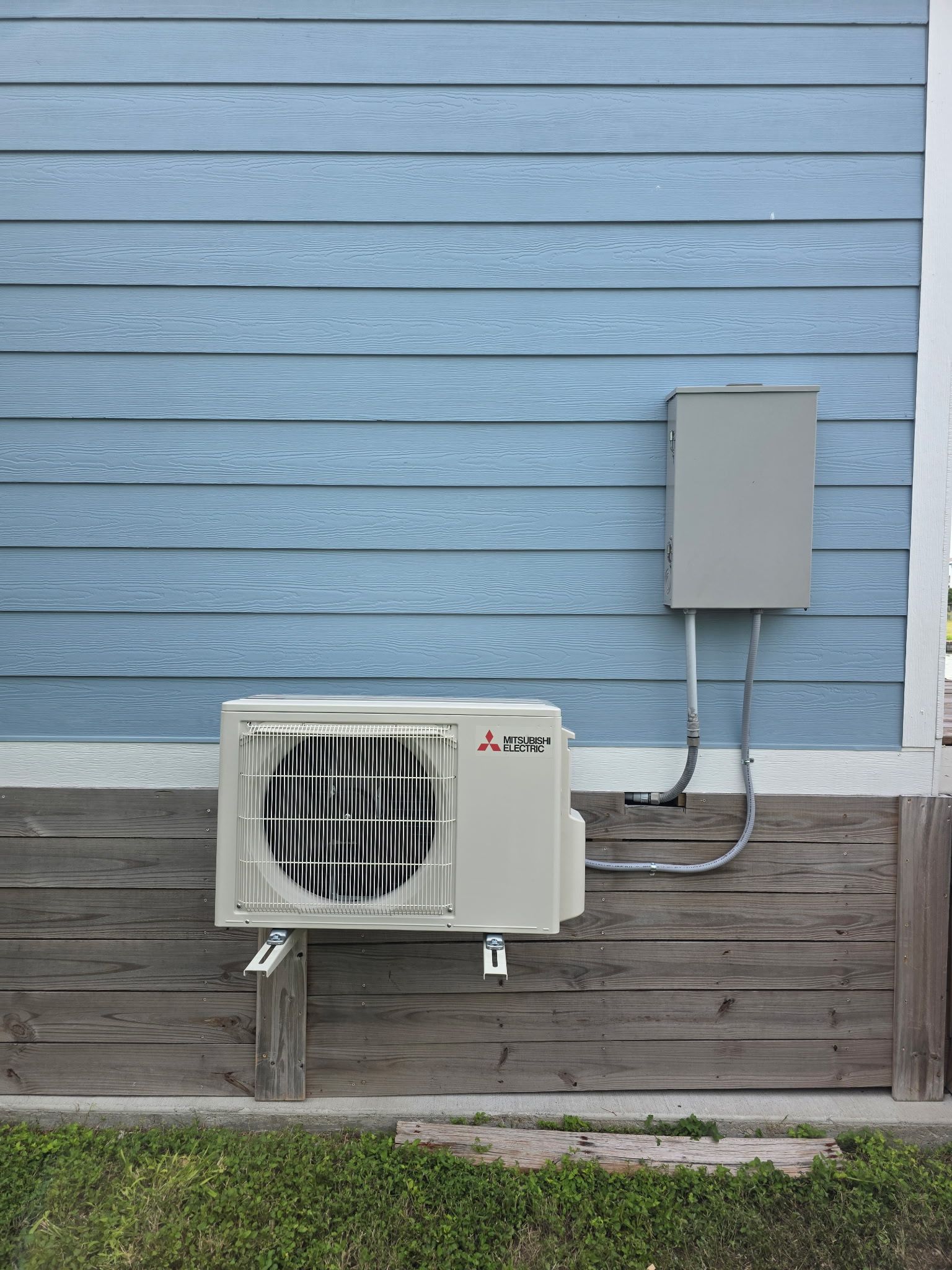 Mitsubishi heat pump unit mounted on blue siding, with an electrical box next to it.