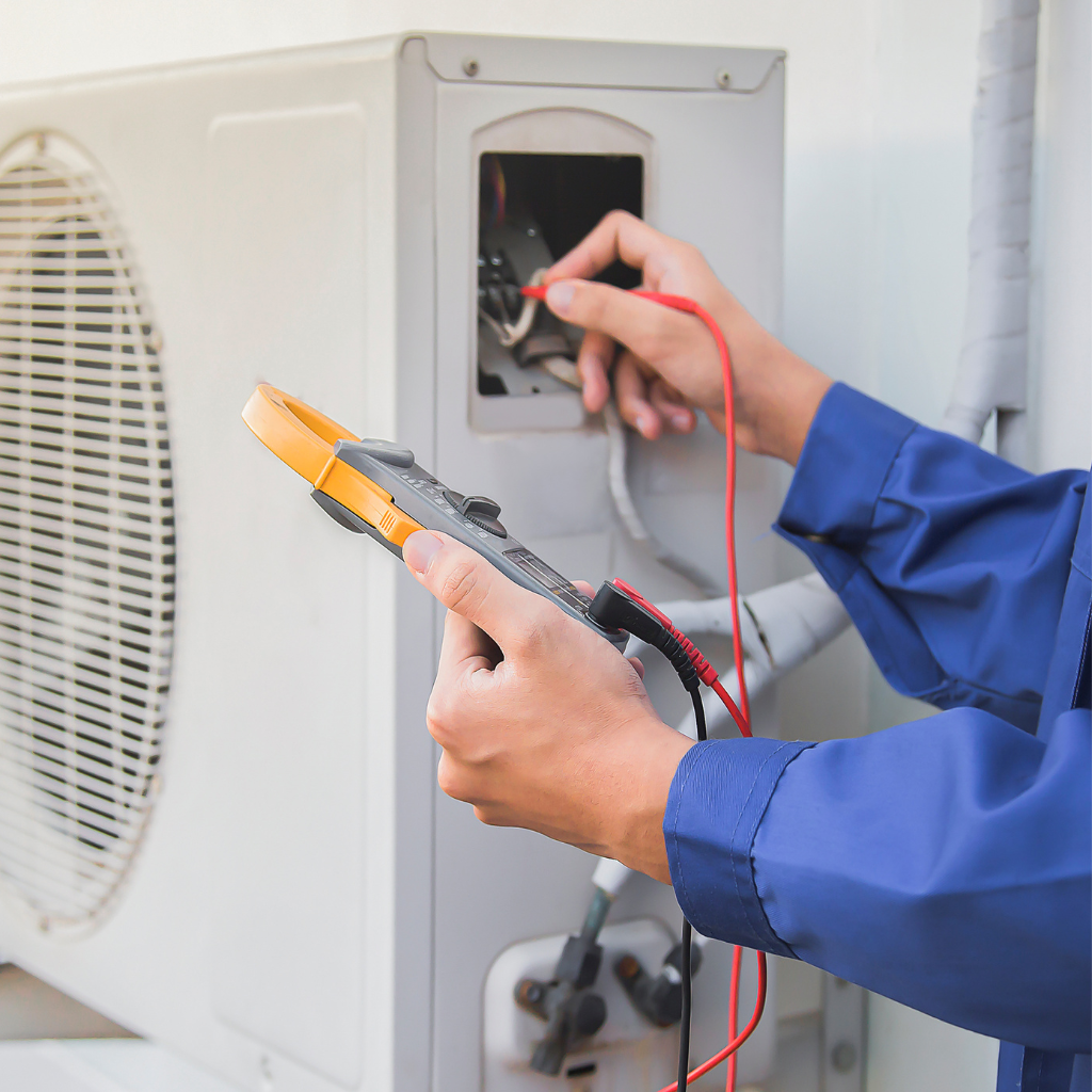 HVAC technician in a blue uniform repairs furnace with a multimeter and flashlight; indoor setting.