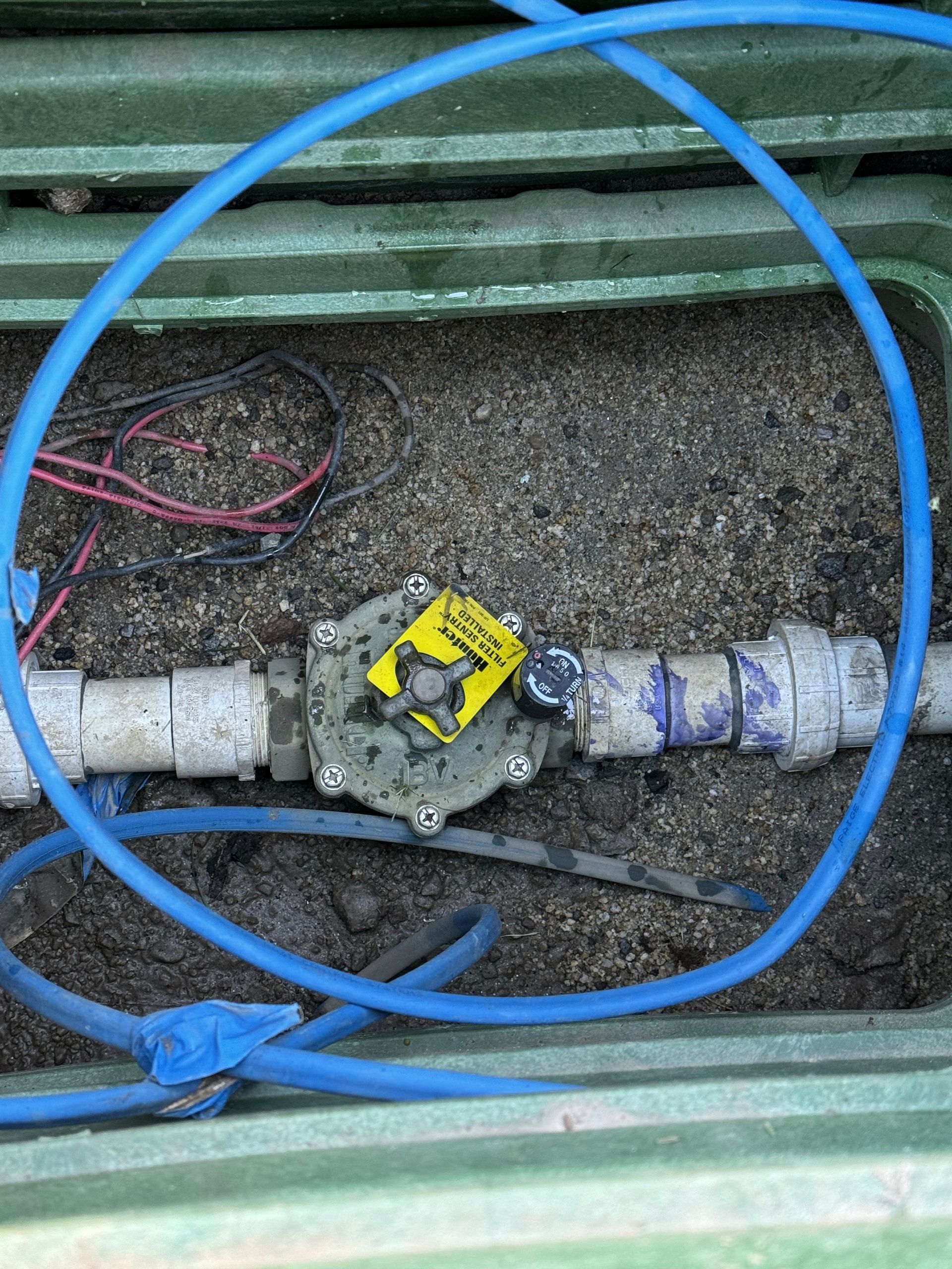 Irrigation valve in a green box with blue tubing and wires.