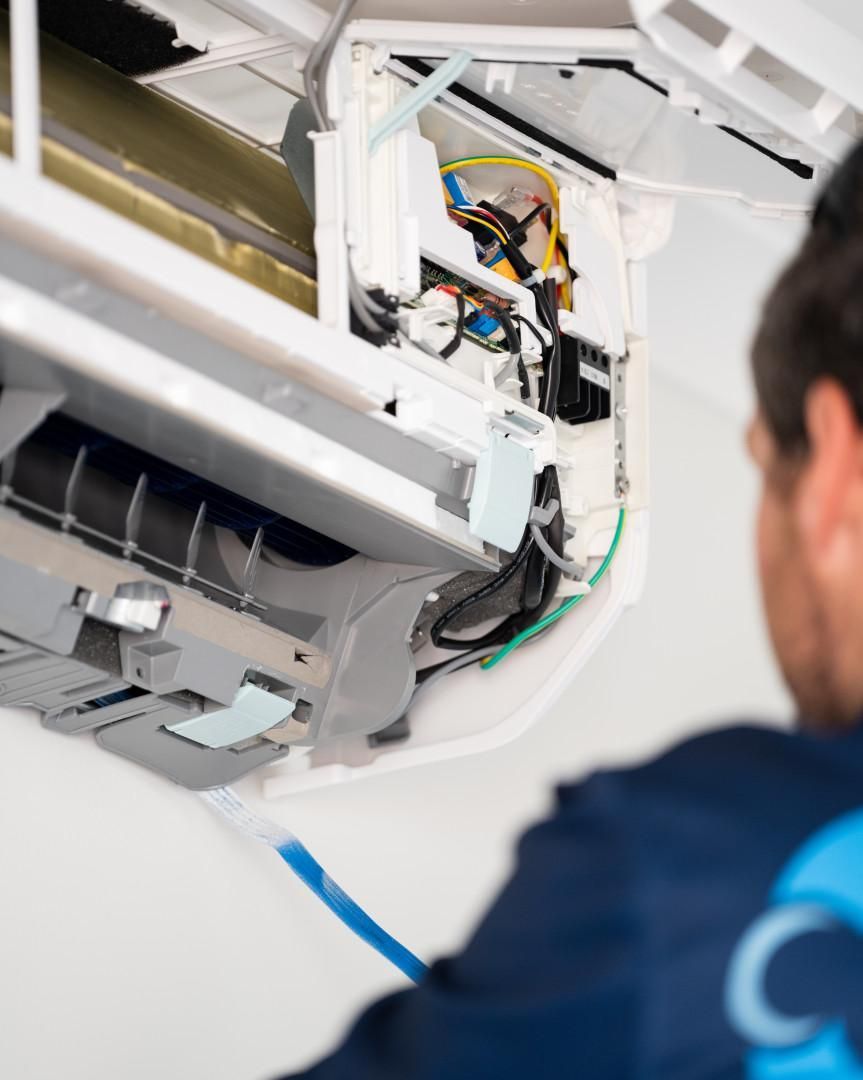 A Man in A Blue Shirt Is Working on An Air Conditioner — Staub Air in Garbutt, QLD
