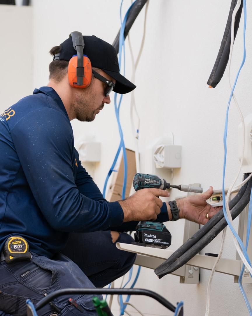 A Man Wearing Headphones and A Hat Is Working with A Drill — Staub Air in Garbutt, QLD