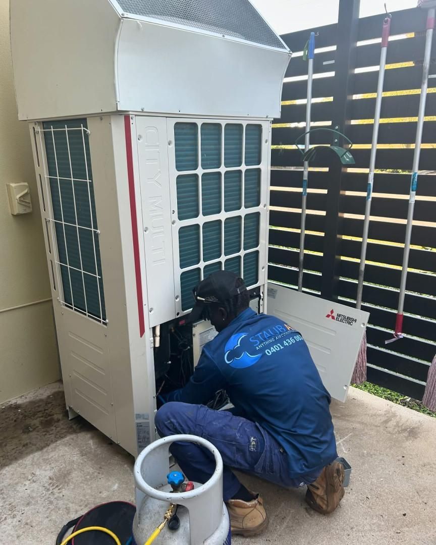 A Man Is Working on An Air Conditioner Outside of A Building — Staub Air in Garbutt, QLD
