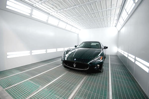 Un coche deportivo negro está aparcado en una cabina de pintura.