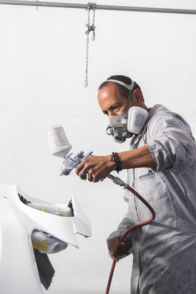 Un hombre que lleva una máscara está pintando con aerosol un objeto blanco.