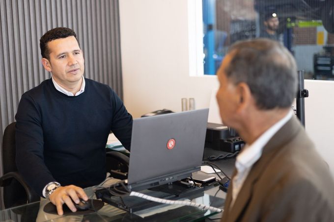 Dos hombres están sentados en un escritorio frente a una computadora portátil.