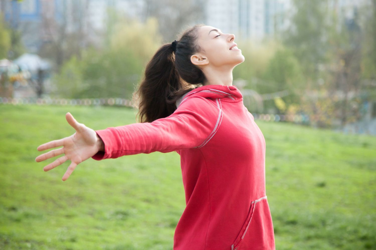 Mujer con una sudadera roja estirando los brazos en un parque