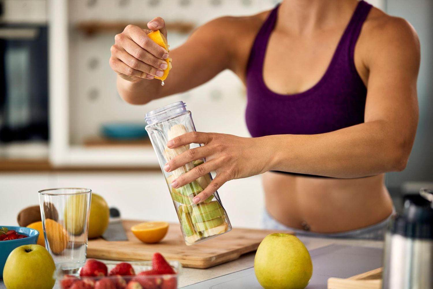 Una persona vierte fruta y semillas en una licuadora en una cocina, con fruta fresca sobre la encimera.