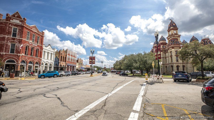Street lined with brick houses and trees; three people in red shirts walking on the road, one with a walker.