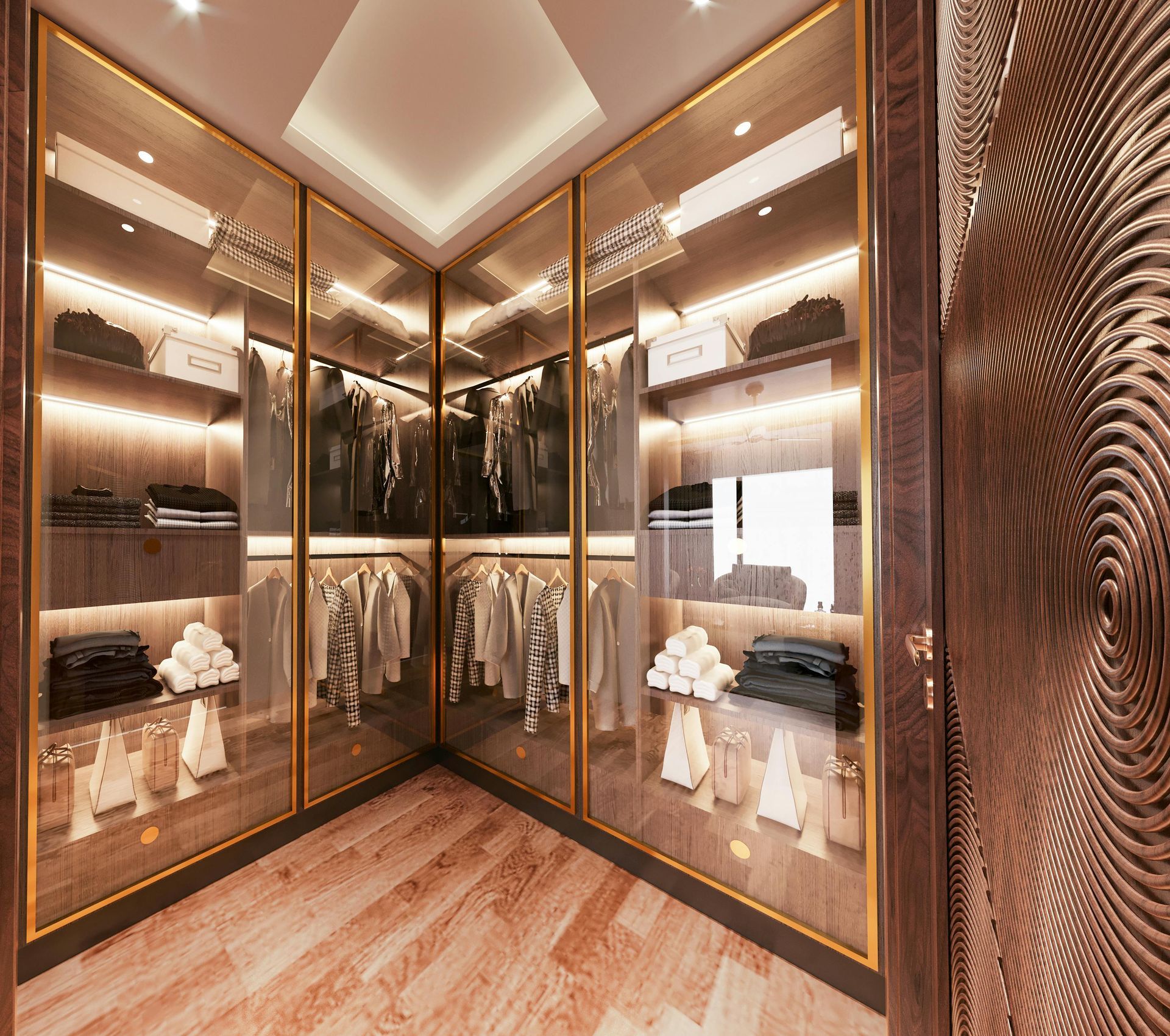 Walk-in closet with glass doors, gold trim, clothes, and shelves with lights, in a room with wood floors.