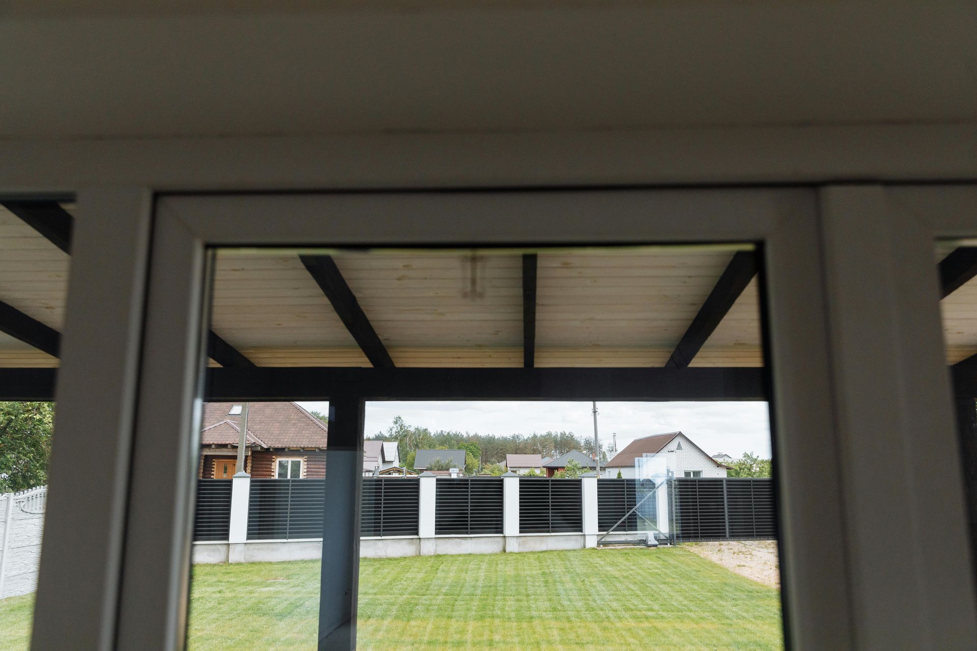 View through a window, showing a backyard with grass, fence, and a partially visible roof.