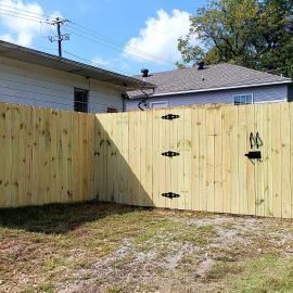 Wooden backyard fence with black hinges and gate, viewed from a grassy yard under a sunny sky
