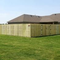 Wooden privacy fence around a backyard beside a house with a shingled roof and green lawn.