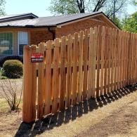 Wooden privacy fence beside a brick house, with a red warning sign attached.