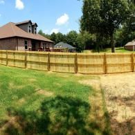 Backyard with a wooden privacy fence, green lawn, and a brick house under trees
