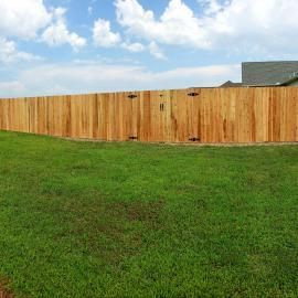 Wooden fence along a green grassy yard under a partly cloudy blue sky