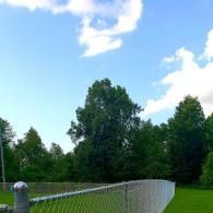 Chain-link fence in a green park under a blue sky with scattered clouds