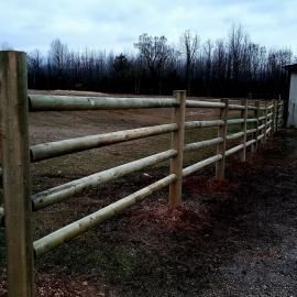 Wooden fence lining a muddy gravel path beside a field under an overcast sky