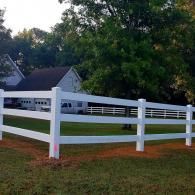 White fenced yard with green grass and a house in the background