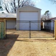 Black metal gate in front of a white garage and beige house in a fenced yard