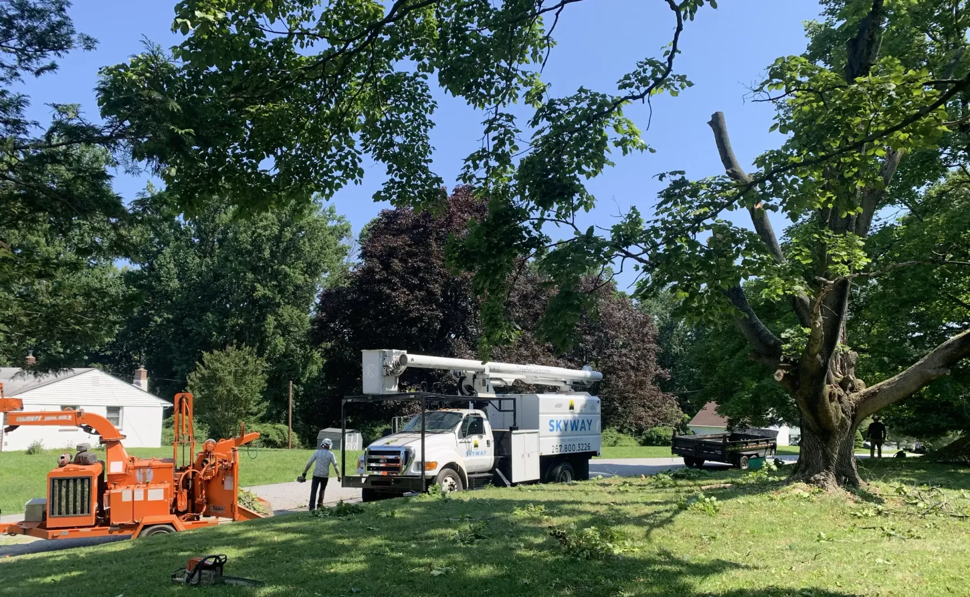 A tree cutting truck is parked in a yard next to a tree chipper.