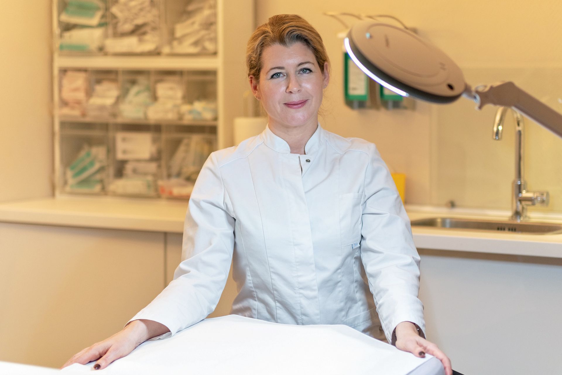 Eine Frau im weißen Kittel sitzt in einem Zimmer auf einem Tisch.