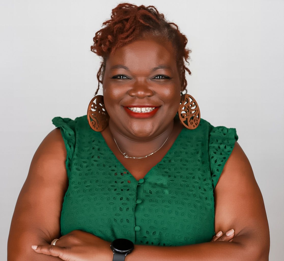 Woman with gray hair and glasses giving a gift with a bow. Balloons in background, brick wall.