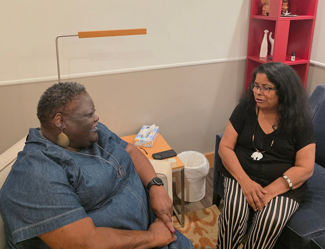 A therapist talking to a couple on a couch, in a well-lit living room setting.