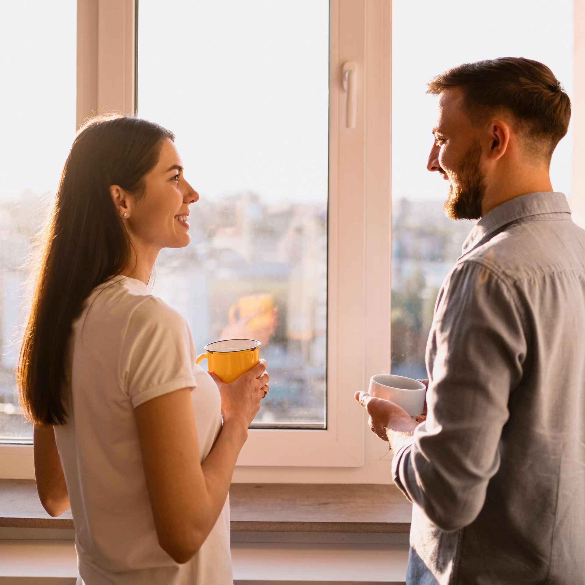 People in a circle, smiling and talking, in a bright room with windows.