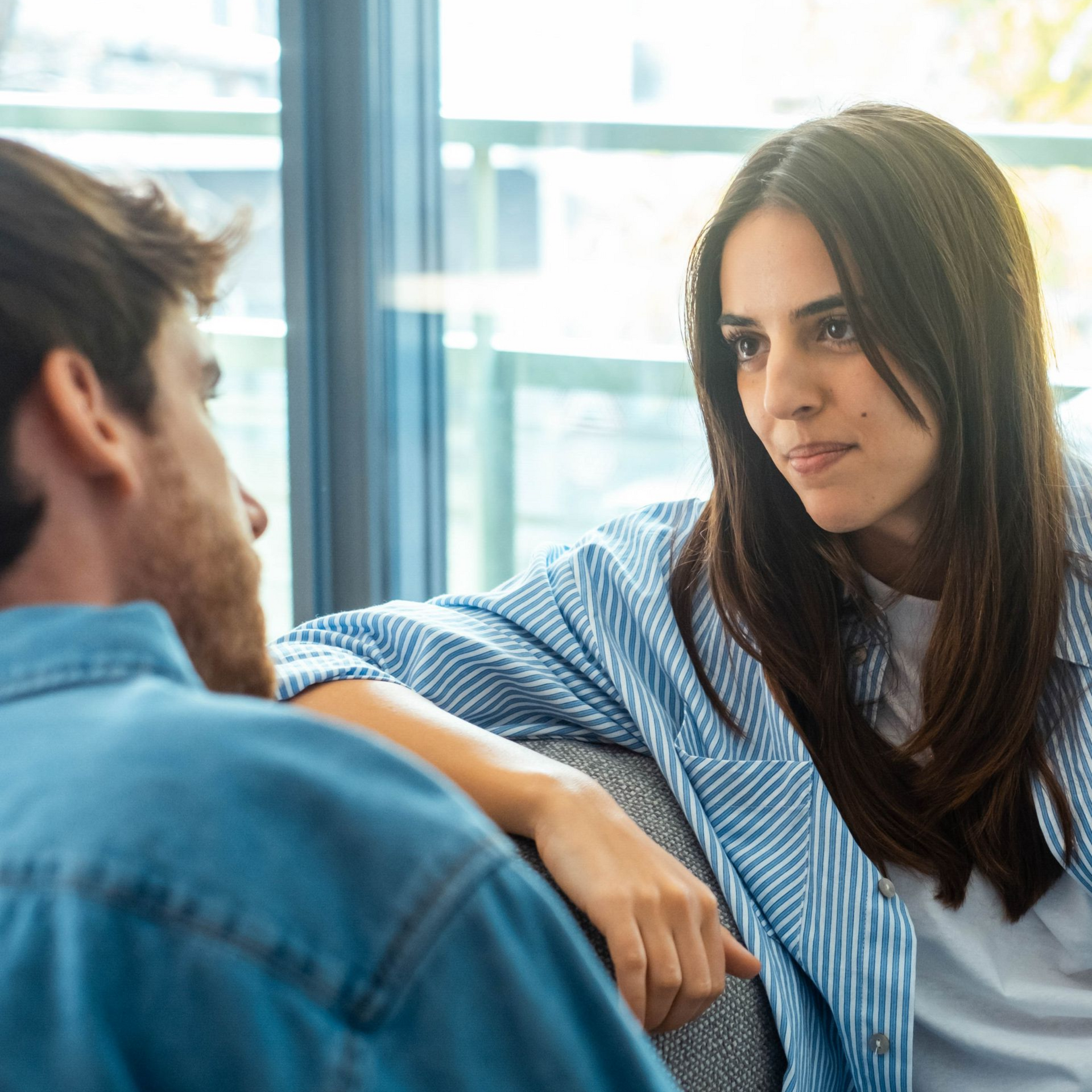 Woman with long brown hair smiling while using a tablet, sitting on a couch. Pink shirt.