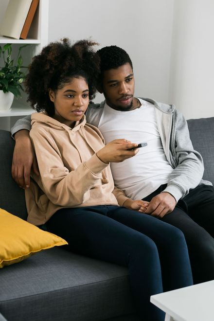 Woman with long brown hair smiling while using a tablet, sitting on a couch. Pink shirt.