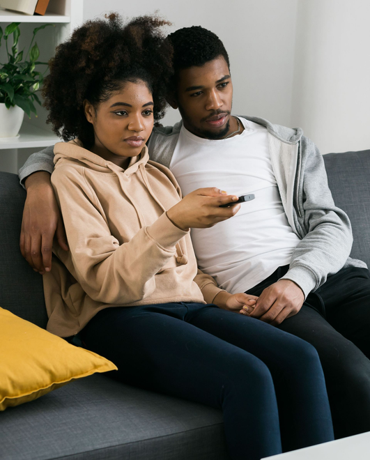Woman with long brown hair smiling while using a tablet, sitting on a couch. Pink shirt.