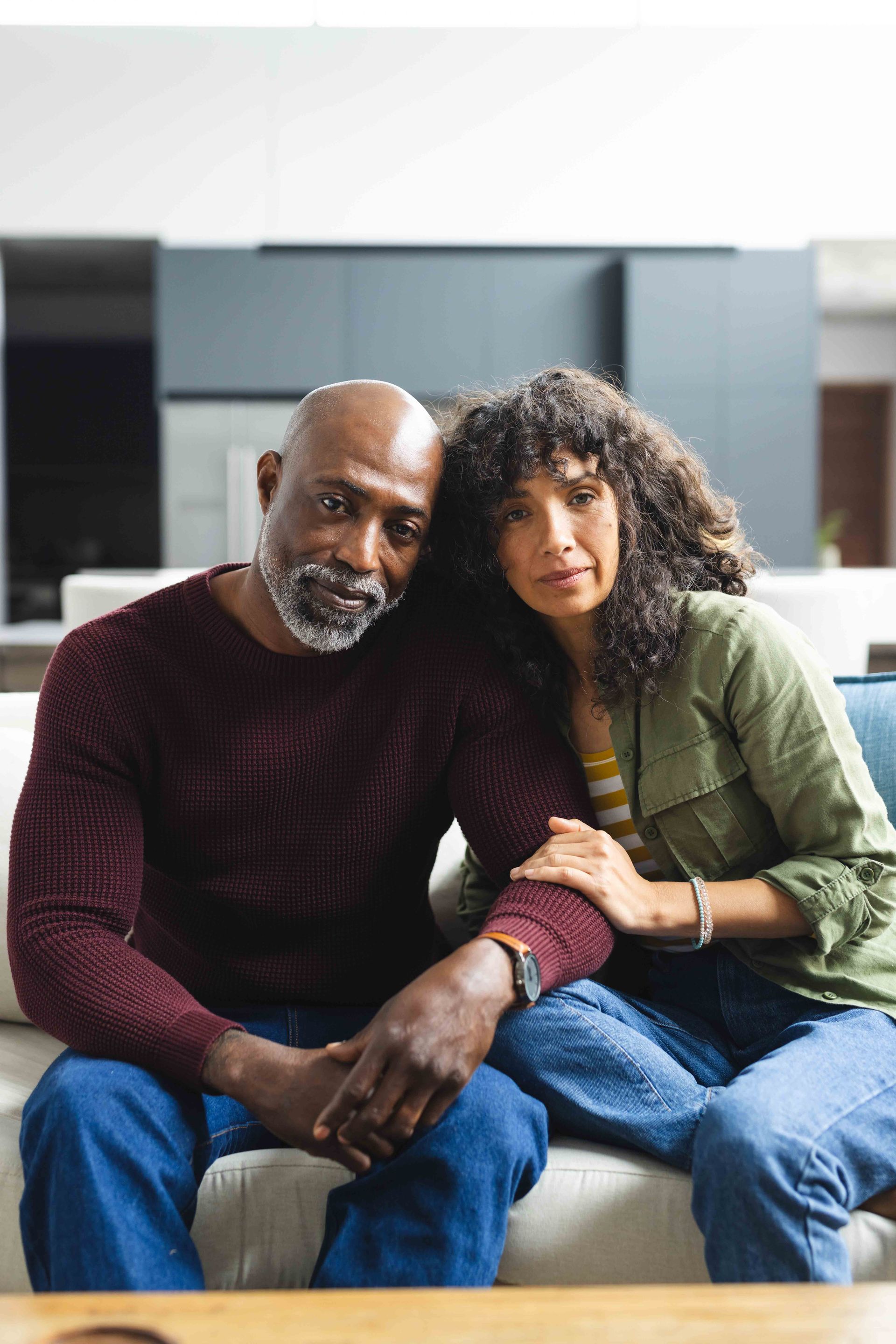 Woman therapist gestures while speaking to a man with tattoos, seated on a couch in an office.